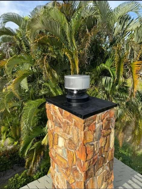 Stone-clad chimney with a black top plate and round metal cap