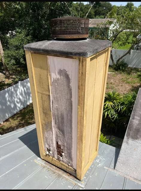 Weathered yellow chimney chase with damaged lower siding and an older metal top